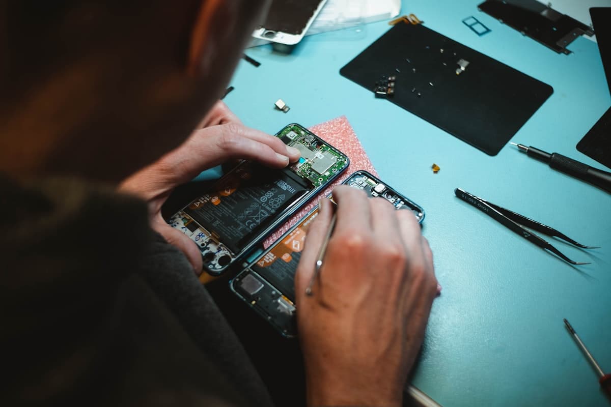 Technician repairing a smartphone with the back panel removed, tools on a workbench